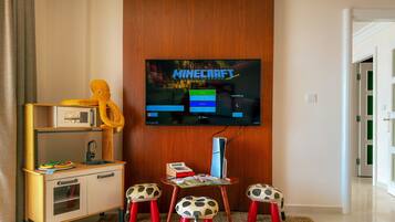 Een kamer met een televisie waarop een spel draait, een bureau met een stoel en een kleine tafel met krukken.