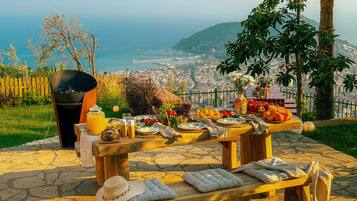An outdoor dining area with a stone table, a fire pit, and a view of a coastal cityscape.