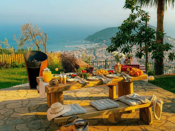 An outdoor dining area with a stone table, a fire pit, and a view of a coastal cityscape. - Qoople Villa Tosсana - Panoramic 360° sea & castle view (Alanya)