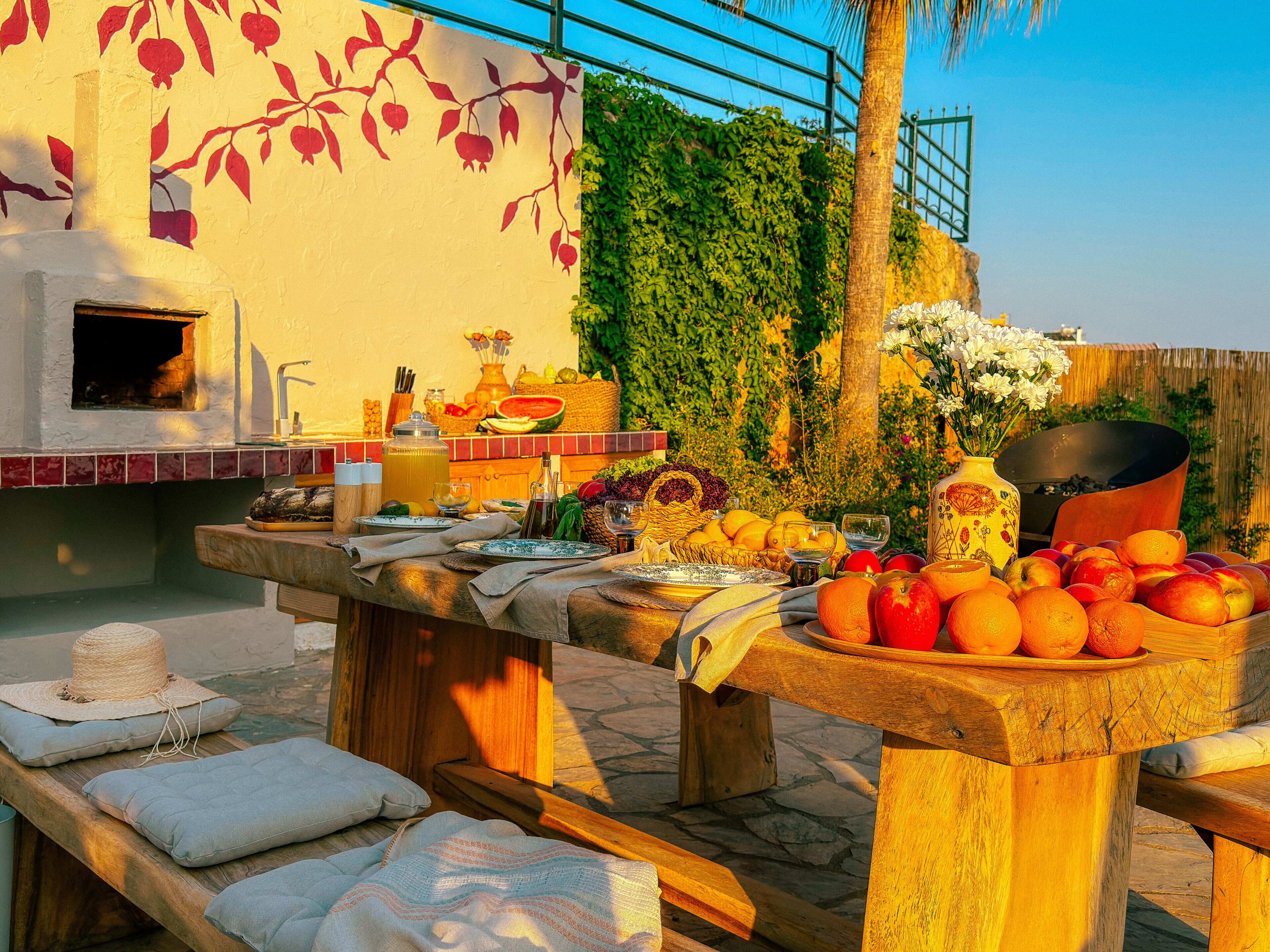 An outdoor dining area with a stone table, wooden benches, and a variety of fruits and vegetables.