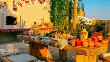 An outdoor dining area with a stone table, wooden benches, and a variety of fruits and vegetables.