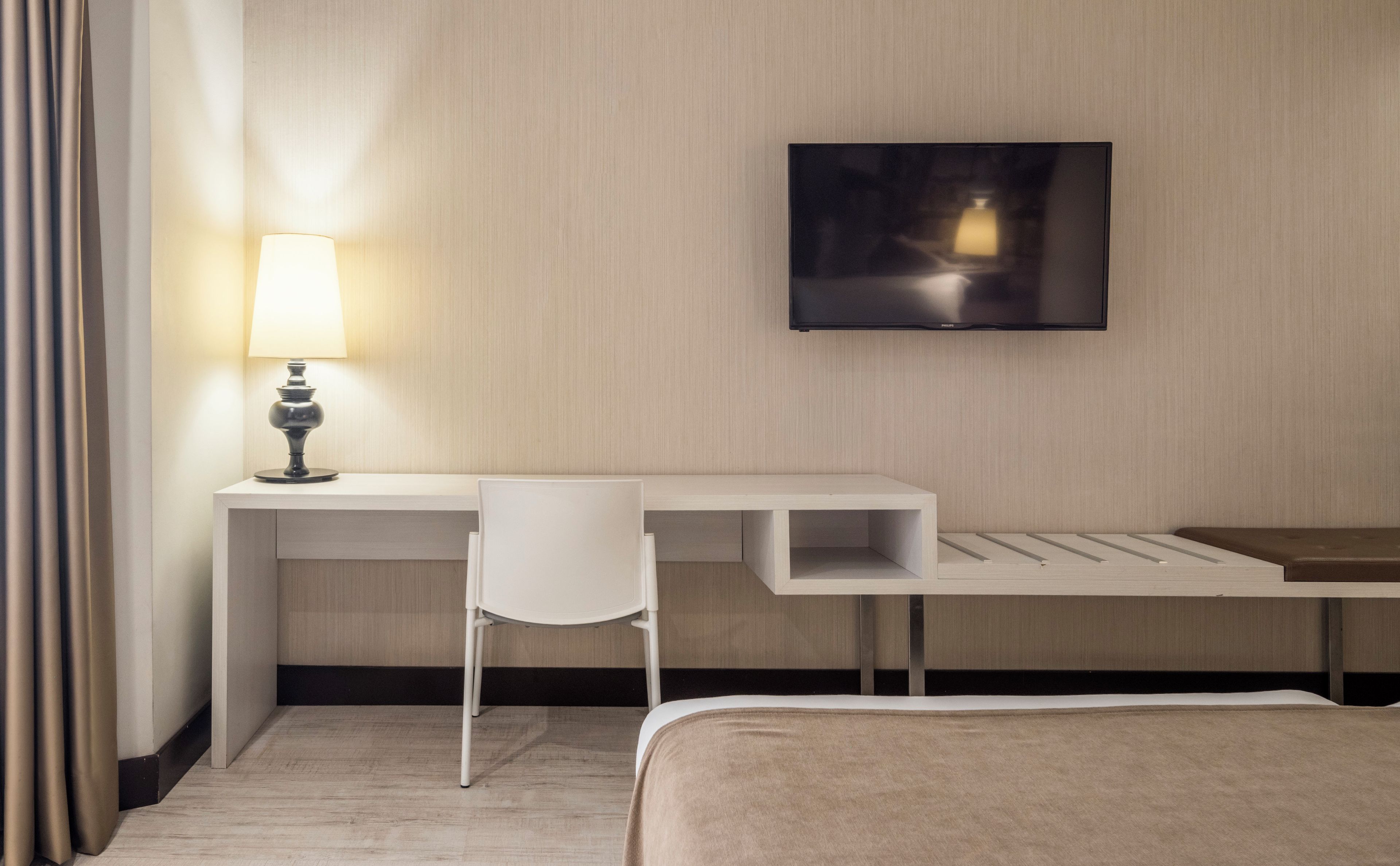 Habitación de hotel con escritorio, silla, cama y televisor de pantalla plana montado en la pared.