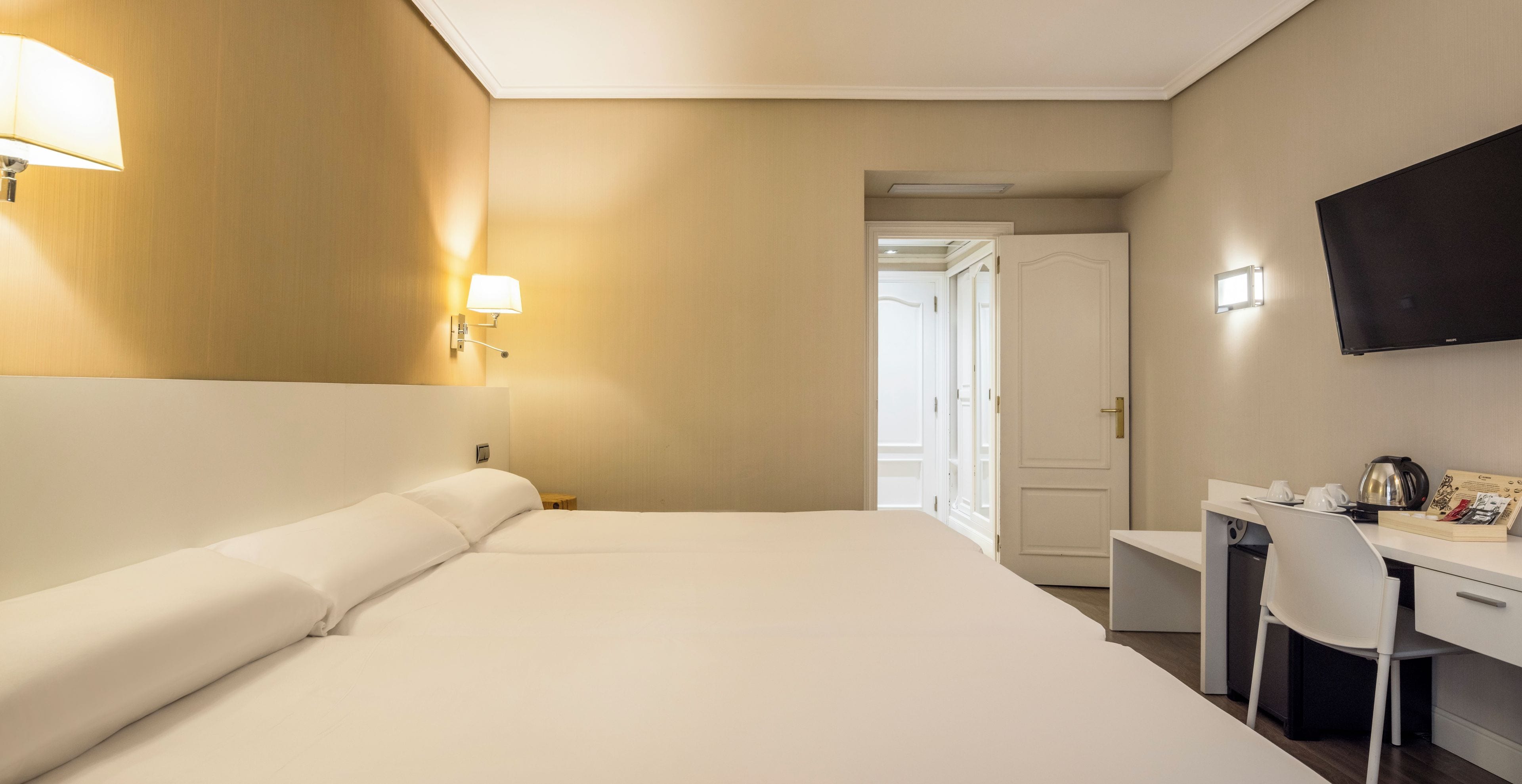 Una habitación de hotel con cama, escritorio, silla y televisión.