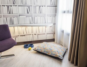 A room with a purple chair, a pet bed, and a bookshelf filled with books. - Hotel ILUNION Abando Bilbao (Bilbao)