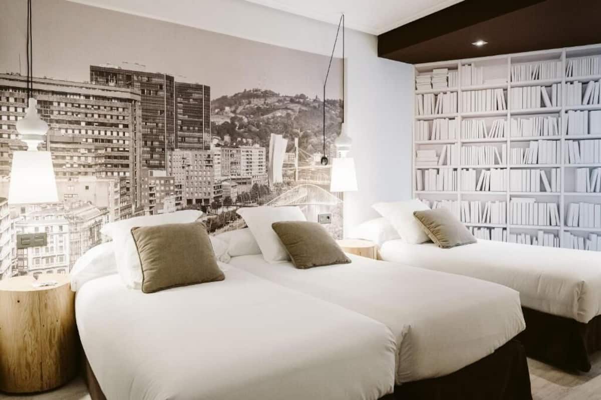 Una habitación de hotel con dos camas, una estantería y un mural con vista a la ciudad.