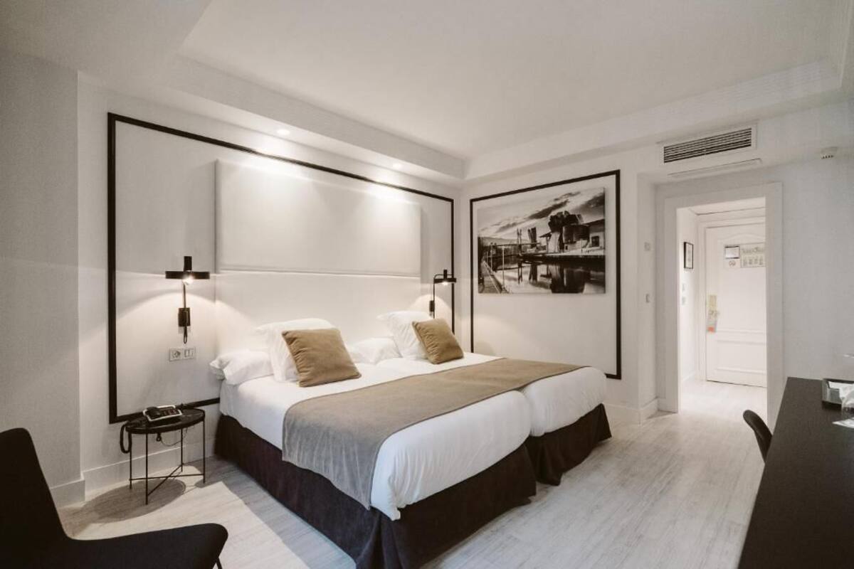 Habitación de hotel moderna con una cama grande, mesitas de noche, un escritorio y un cuadro enmarcado en la pared.
