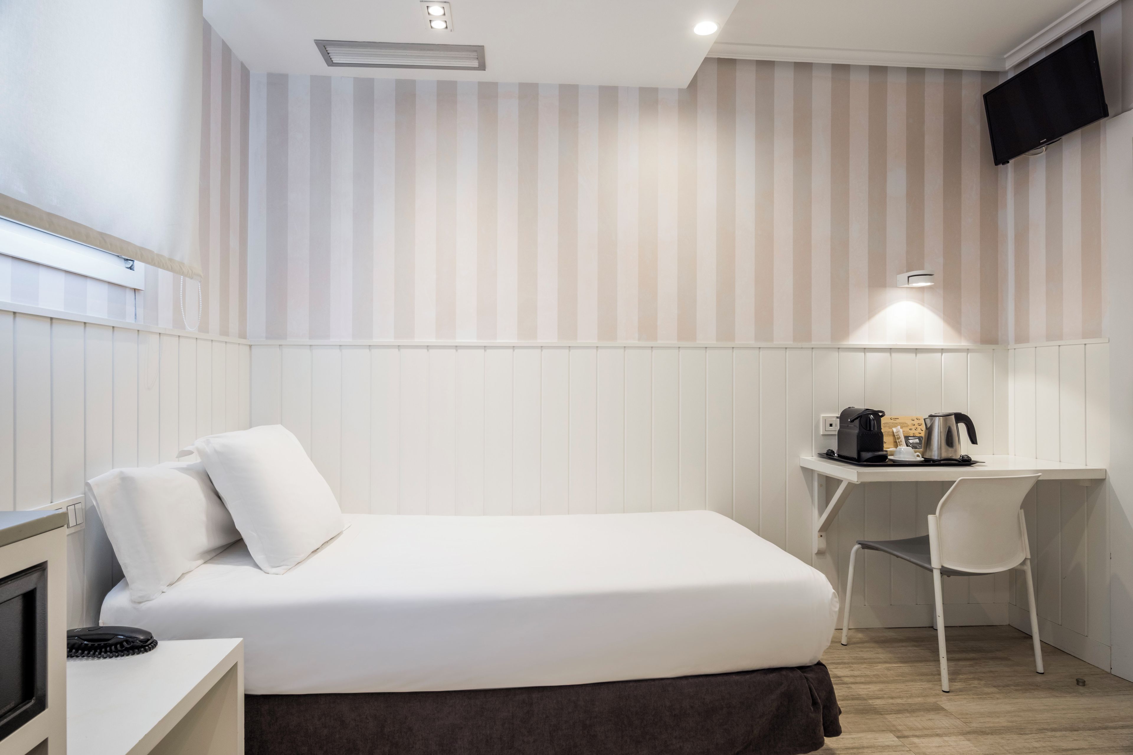 Una habitación de hotel con una cama, un escritorio, una silla, un televisor y una cafetera.