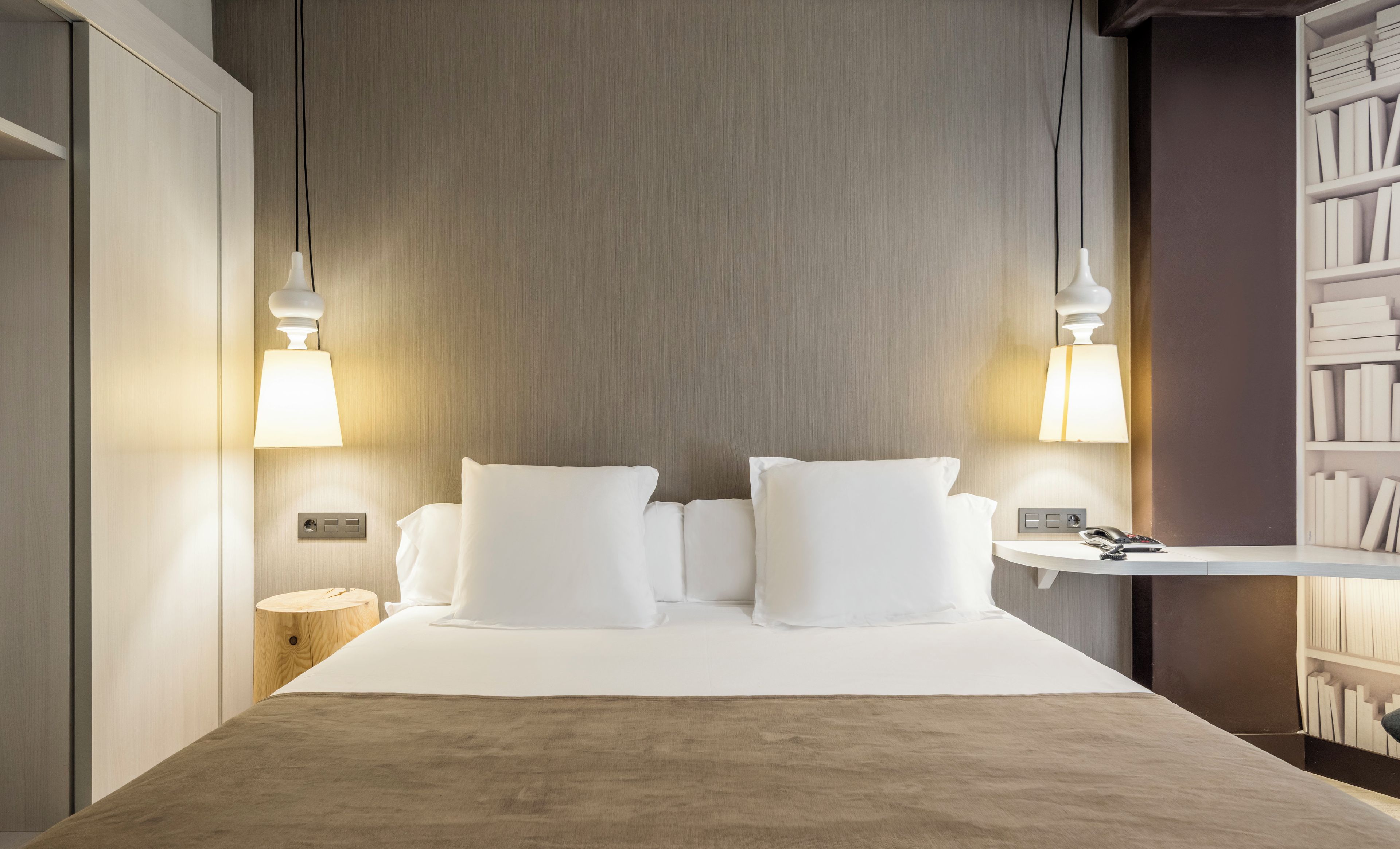 Una habitación de hotel con una cama, lámparas de noche, una mesita de noche y una estantería.