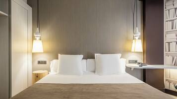 Una habitación de hotel con una cama, lámparas de noche, una mesita de noche y una estantería.