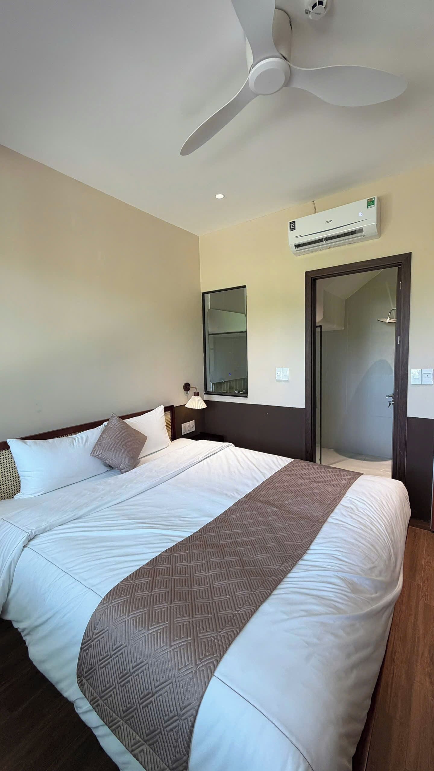Une chambre d’hôtel équipée d’un lit, d’un ventilateur de plafond, d’un climatiseur, d’un miroir et d’une porte donnant accès à une douche.
