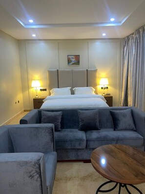 A hotel room with a bed, two bedside lamps, a sofa, a coffee table, and a painting on the wall. - Eduardo Hotel Abuja (Abuja)