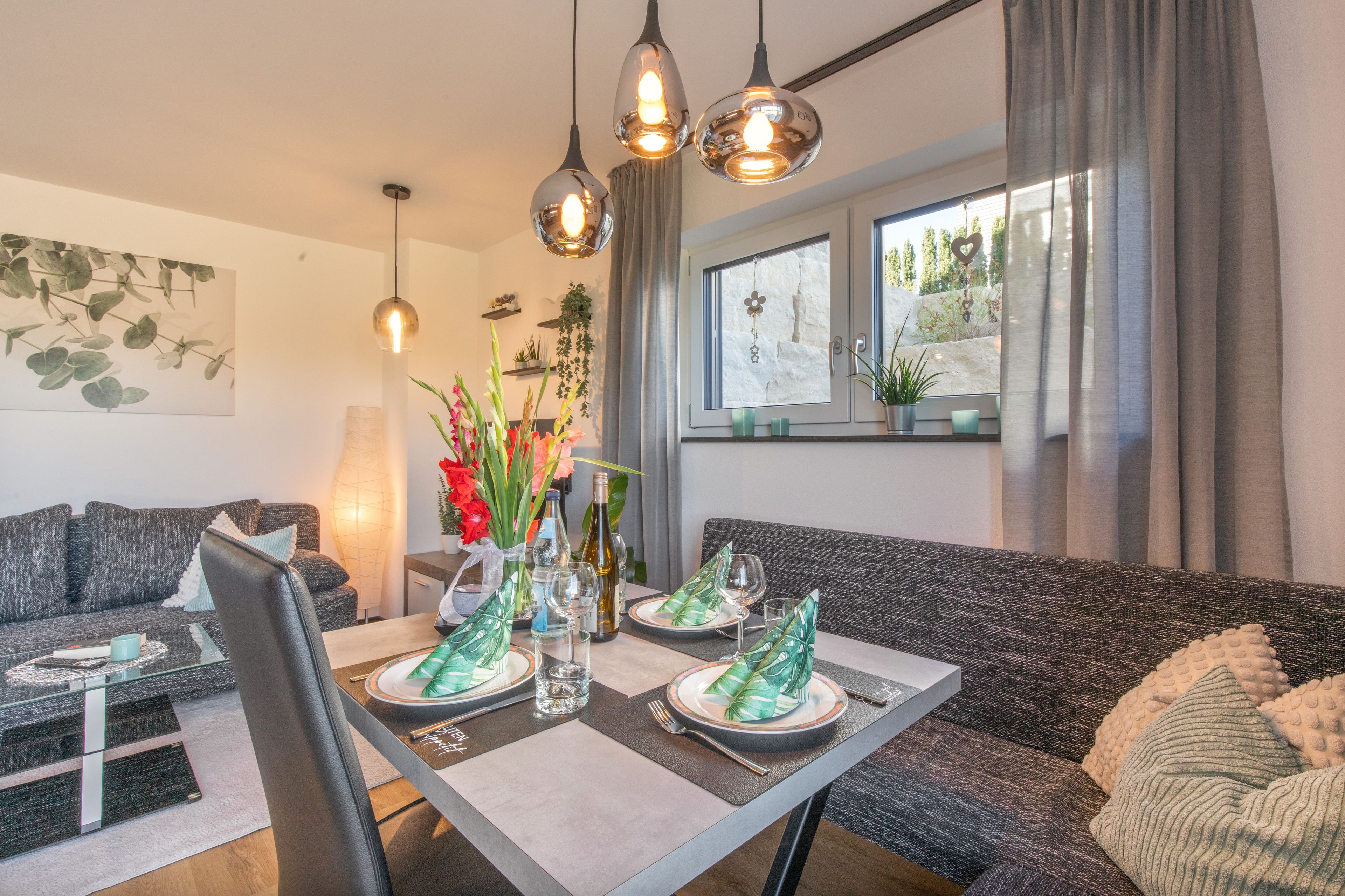 Een moderne woonkamer met een eettafel gedekt voor twee personen, een bank en een raam met uitzicht.