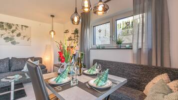 Een moderne woonkamer met een eettafel gedekt voor twee personen, een bank en een raam met uitzicht.