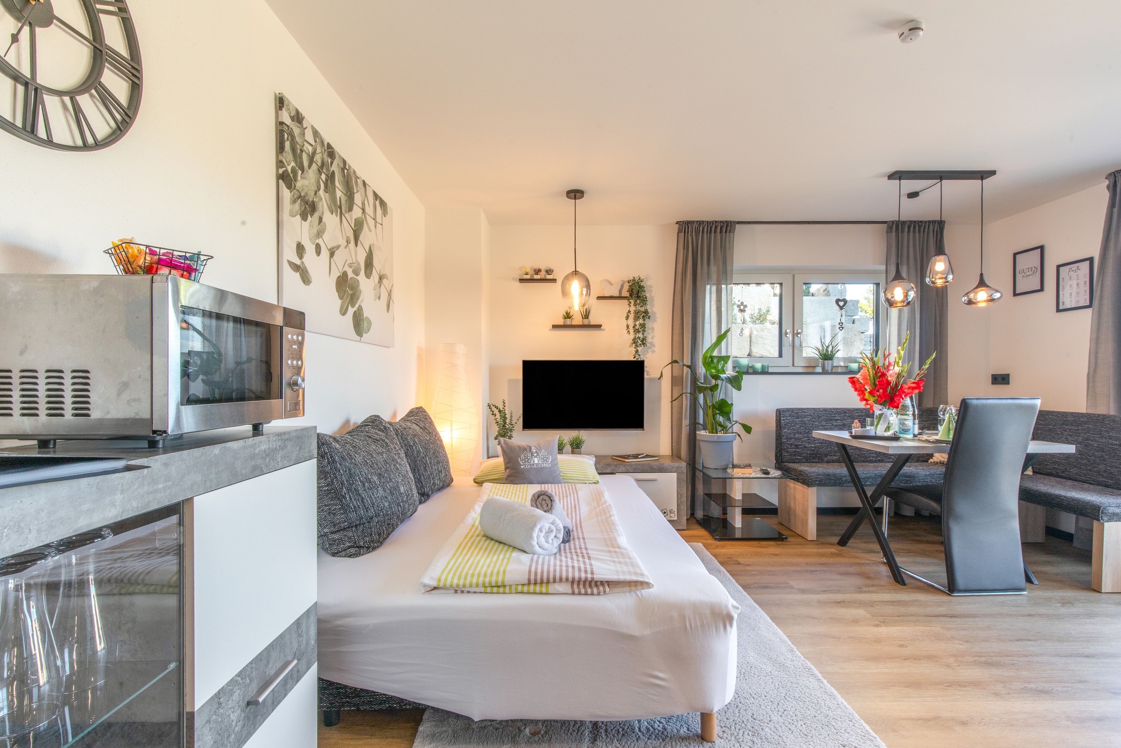 Een moderne woonkamer met een bank, een eettafel met stoelen, een flatscreen televisie en een keukenhoek met een magnetron.