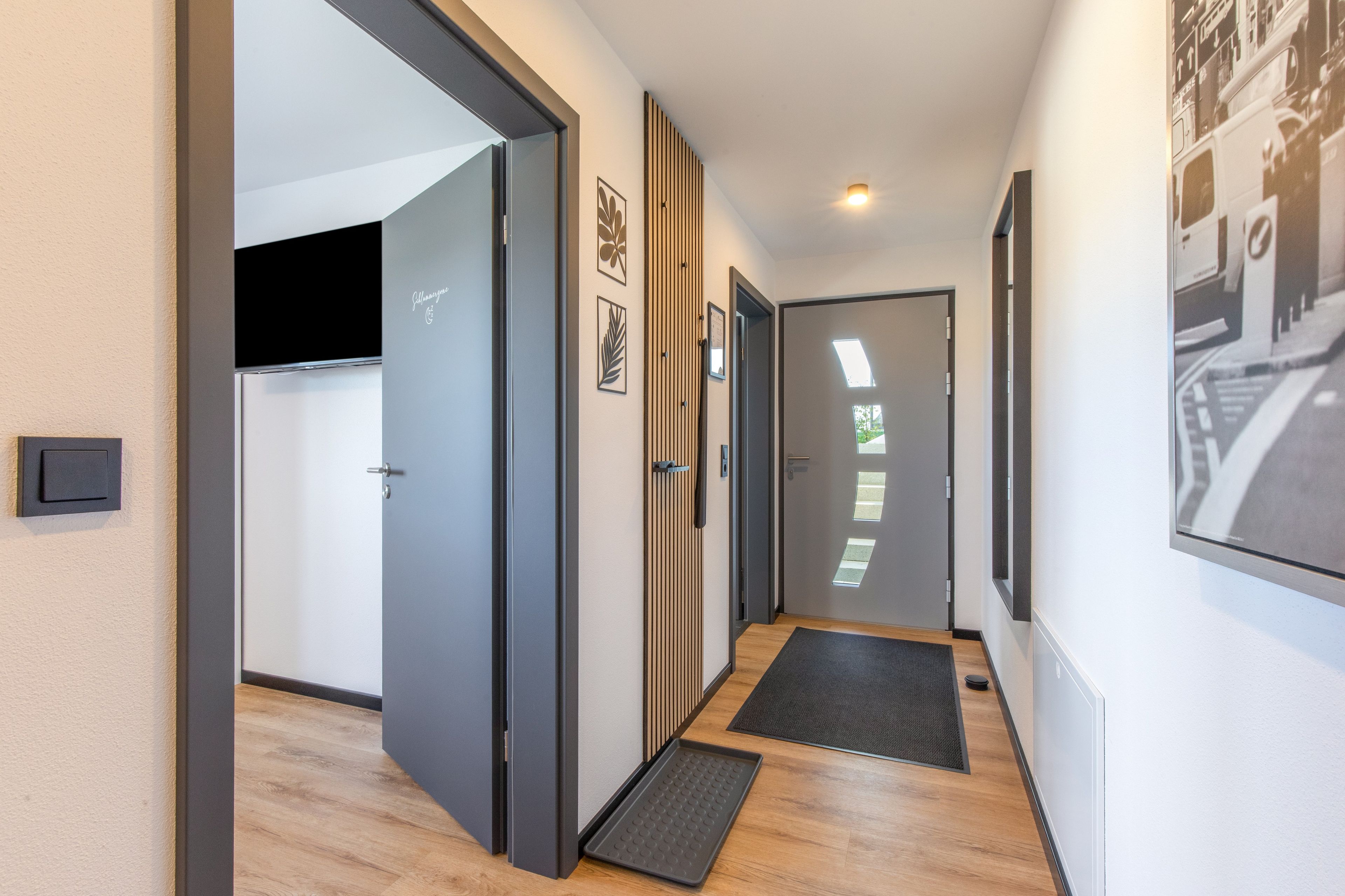 A hallway with a door leading to a room, a wall-mounted light fixture, and a door with a window.