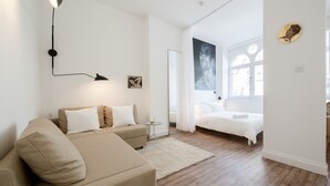 Ett modernt sovrum med en säng, en soffa, ett litet bord och en vägglampa.