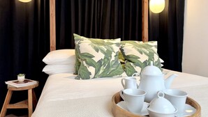 En seng med himmelseng, to puder med bladmotiver, et bakke med hvide tekopper og et thekande, samt en lille træskammel med en plante.