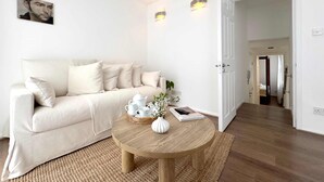En minimalistisk stue med en sofa, et rundt træbord og en dør til et andet rum.