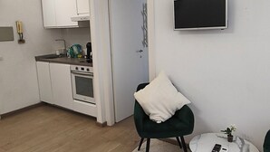 Ein kompakter Wohnbereich mit Küchenzeile, einer Essecke mit kleinem Tisch und Stuhl sowie einem an der Wand befestigten Fernseher.