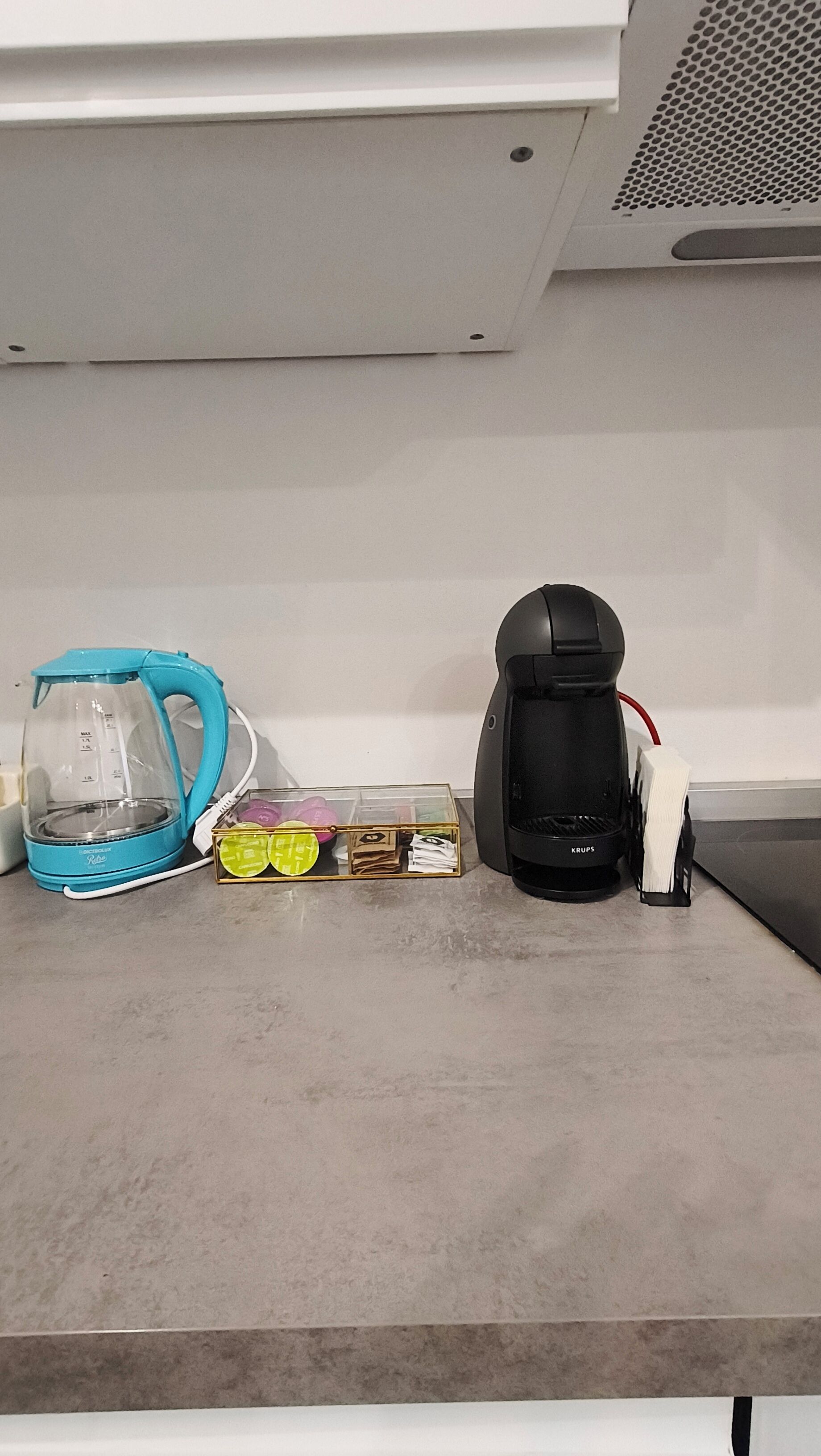 A kitchenette with a coffee maker, a kettle, and a small storage box.