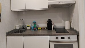 Eine kleine Küche mit weißen Schränken, einem Spülbecken, einem Herd und einer Arbeitsplatte mit verschiedenen Gegenständen.