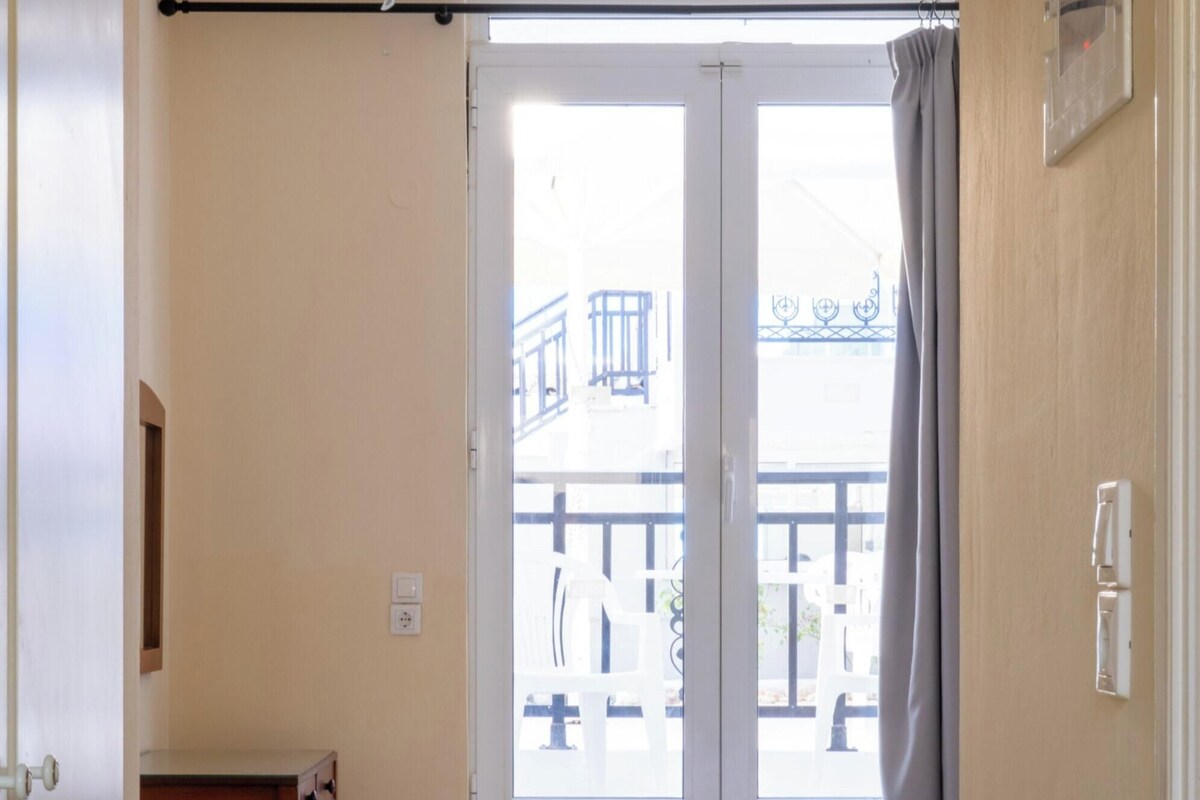 Habitación de hotel con cama, escritorio y ventana con vistas al balcón exterior.