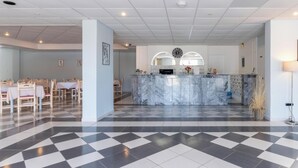 Un vestíbulo de hotel con piso a cuadros, un mostrador de recepción de mármol y un comedor con mesas y sillas.