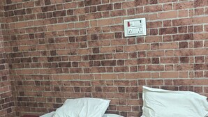 Una habitación con pared de ladrillo, dos camas con sábanas blancas, una manta roja sobre la cama inferior y un enchufe en la pared.