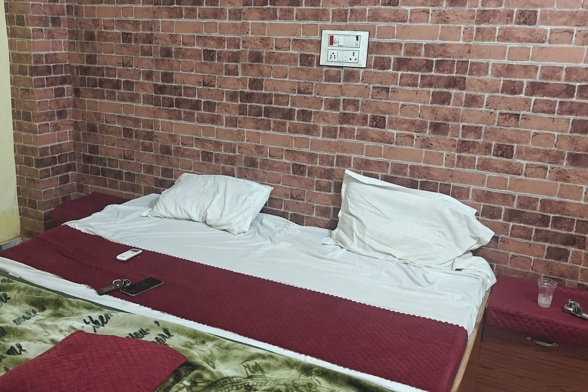 A single bed with a red blanket, a bedside table with a glass, and a brick wall.