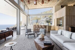 Een moderne woonkamer met een groot raam, een bank, fauteuils, een salontafel en uitzicht op de oceaan.