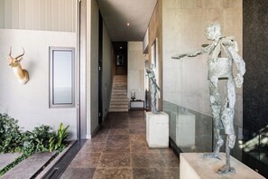 Un couloir orné d’une tête de cerf accrochée au mur, d’une sculpture représentant un squelette et, au fond, d’un escalier.
