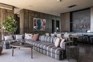 Ein modernes Wohnzimmer mit einem Ecksofa, einem Couchtisch und einem Essbereich, im Hintergrund ist eine Küche zu sehen.