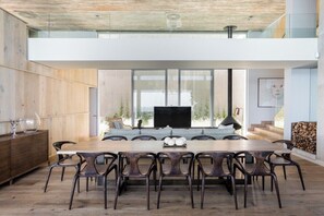 A modern dining area with a large wooden table and chairs, a television, and a view of the outdoors. - Obsidian (Cape Town)