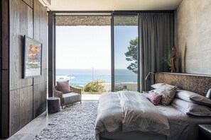 Een slaapkamer met een groot bed, uitzicht op de oceaan en een schuifdeur naar een buitenruimte.