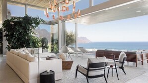 Ein modernes Wohnzimmer mit großem Fenster und Meerblick, einer Couch, Sesseln und einem Couchtisch.