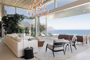 A modern living room with a large window overlooking the ocean, a sofa, chairs, and a coffee table. - Obsidian (Cape Town)