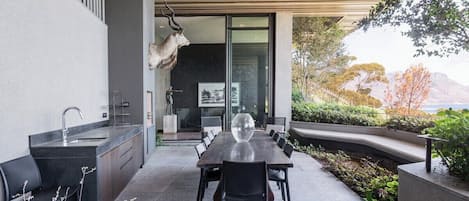 A modern outdoor dining area with a long table and chairs, a built-in kitchen with a sink, and a decorative antler sculpture.