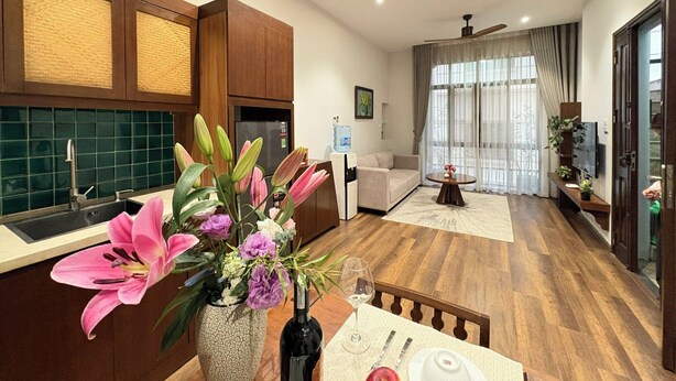 A modern living room with a dining area, a kitchen with green tiles, wooden cabinets, and a large window with curtains. - Satori1 Apartment (Hanoi)
