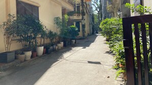 A narrow street with buildings on either side, potted plants lining the sidewalks, and a motorbike parked on the right. - Satori1 Apartment (Hanoi)