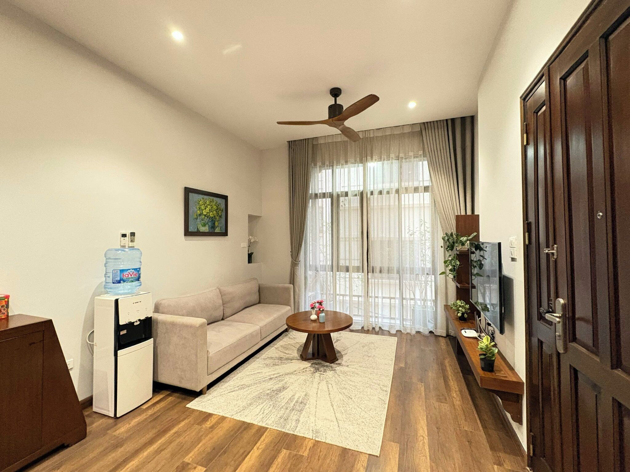 A living room with a sofa, a coffee table, a ceiling fan, a water dispenser, and a TV.