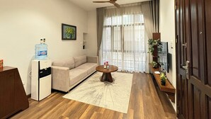 A living room with a sofa, a coffee table, a ceiling fan, a water dispenser, and a TV. - Satori1 Apartment (Hanoi)