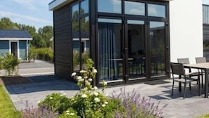 A modern house with a glass conservatory, a patio with outdoor furniture, and a garden with flowers. - Holiday Home in Nijkerk With Terrace (Nijkerk)