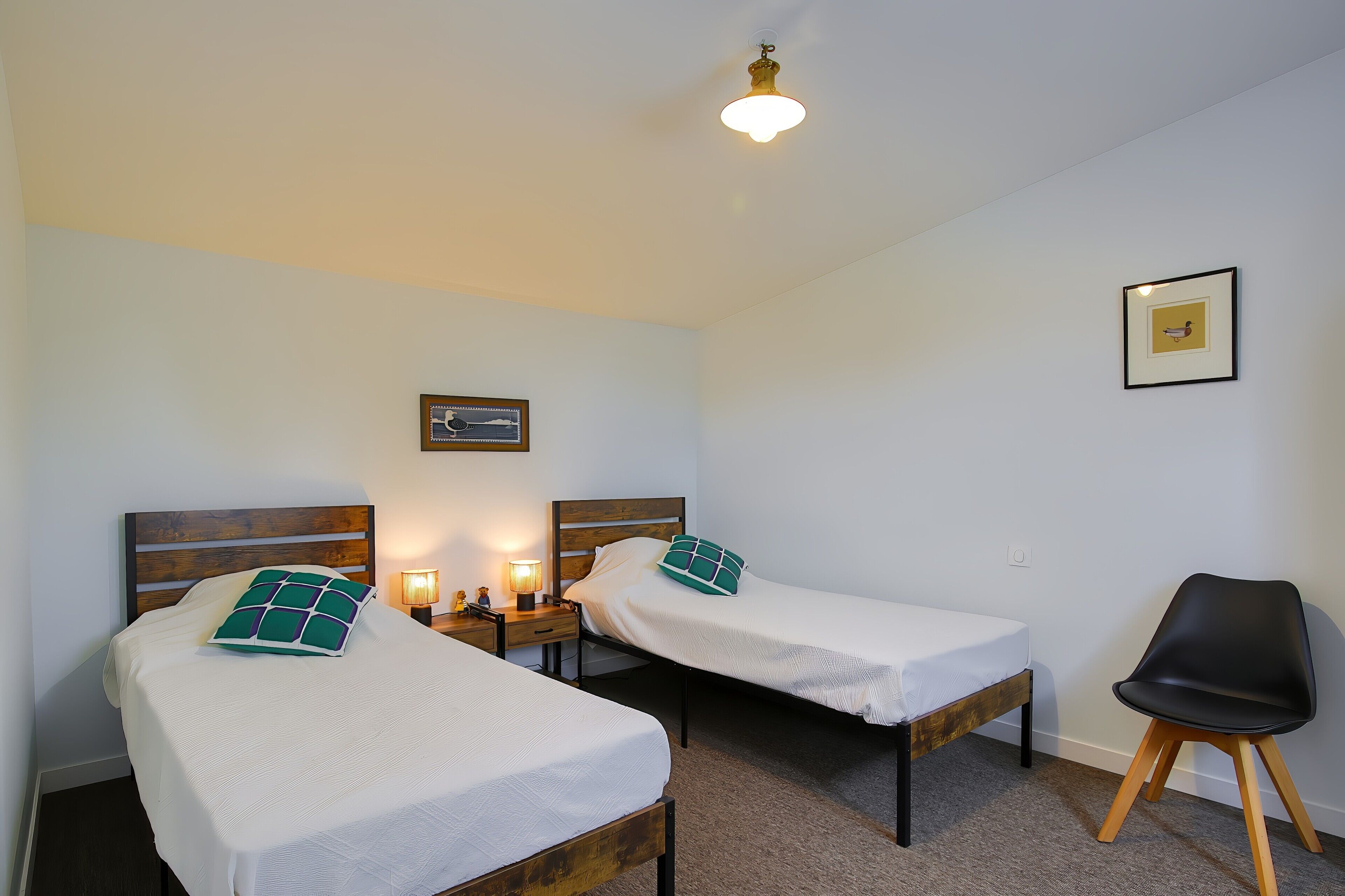 Ein Zimmer mit zwei Einzelbetten, einem Nachttisch mit Lampe, einem Sessel und einem gerahmten Bild an der Wand.