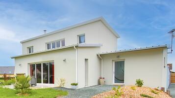 Une maison moderne à deux étages, dotée d’une grande porte-fenêtre coulissante, d’un petit porche et d’une allée gravillonnée.