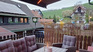 Un espace extérieur aménagé avec des meubles en osier et une table, offrant une vue sur un village aux maisons traditionnelles et une colline en arrière-plan.