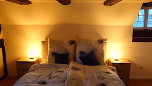 Une chambre à coucher avec un lit, deux tables de chevet avec des lampes, des poutres en bois au plafond et une fenêtre.