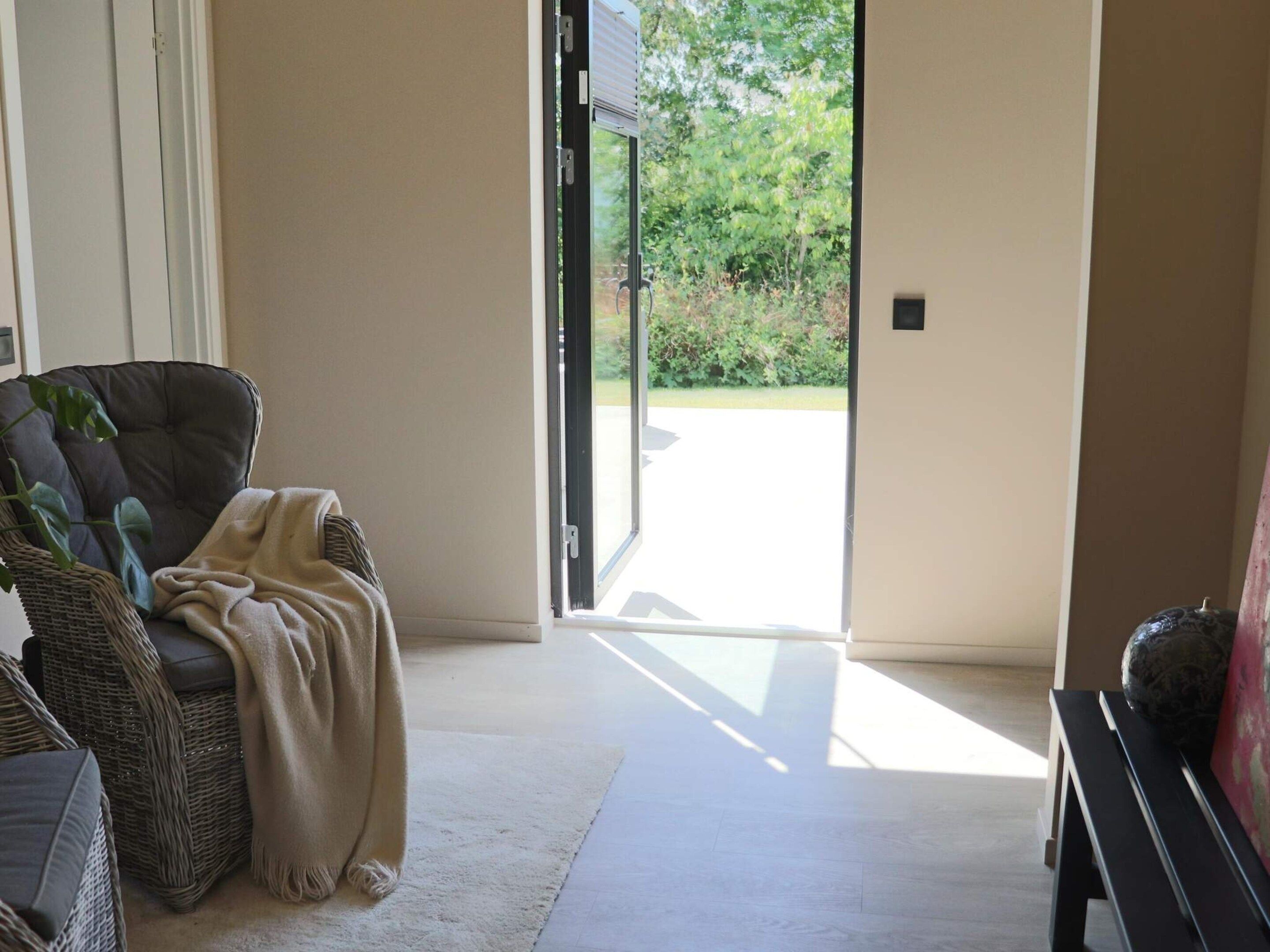 Una habitación con una silla de mimbre, un banco y una puerta que da al exterior.