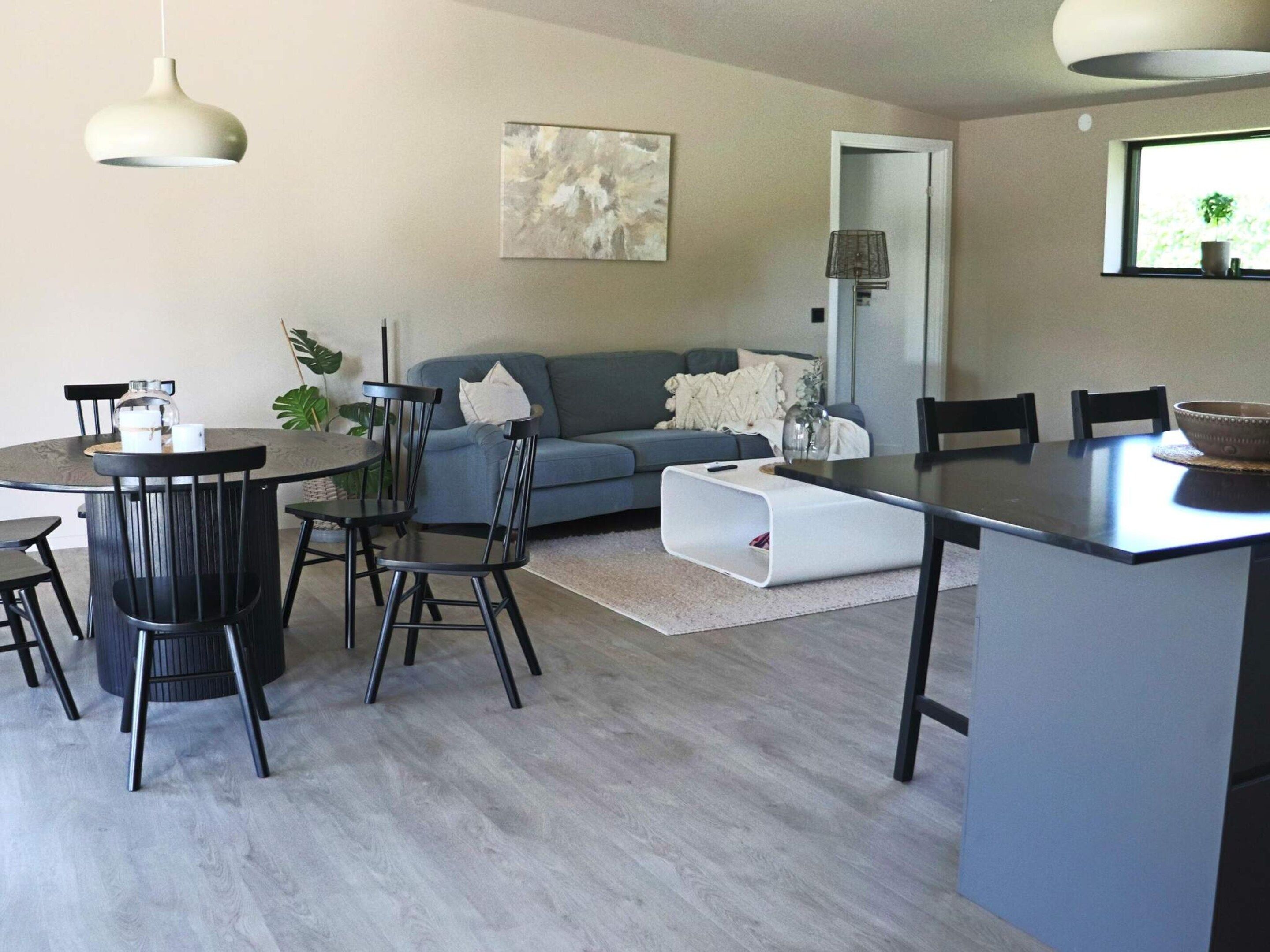 A modern living room with a grey sofa, a dining table with chairs, and a kitchen area with a countertop.