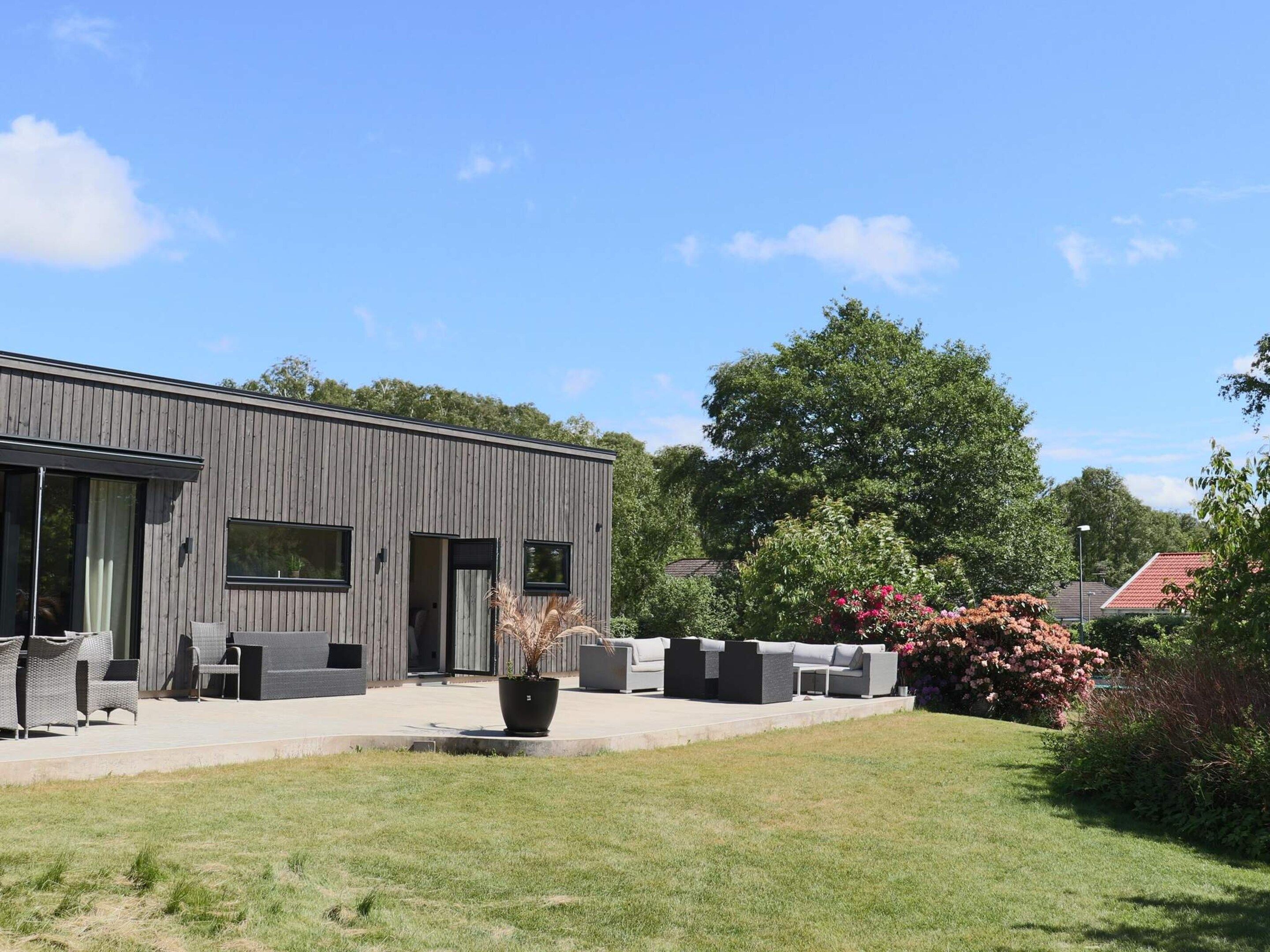 A modern building with a flat roof, large windows, and a paved patio area with outdoor furniture.