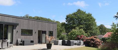 A modern building with a flat roof, large windows, and a paved patio area with outdoor furniture.